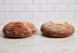 Two boules of baked bread next to each other, one with more even browning